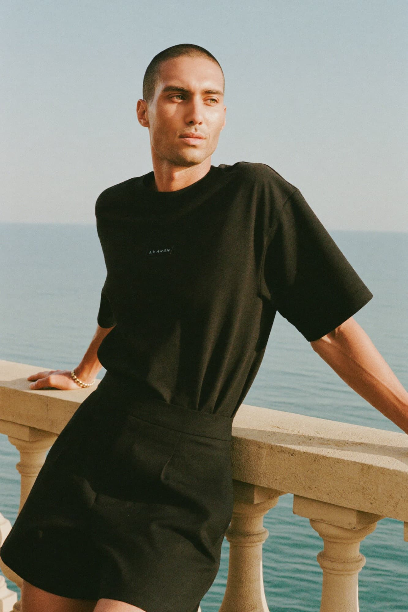 Model in an all-black heavyweight tee at a sun-drenched Mediterranean balustrade, golden hour