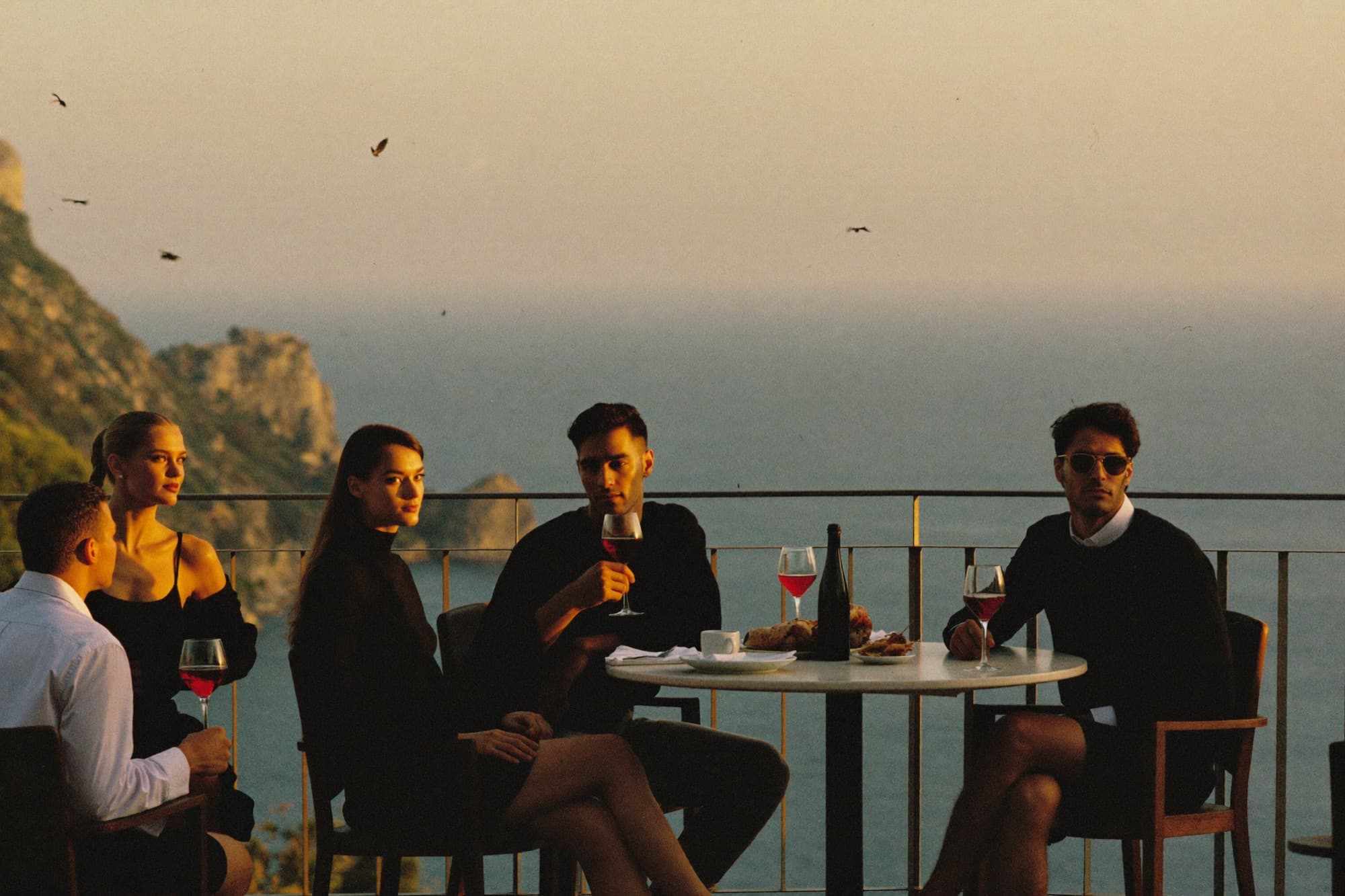 Friends in minimal black essentials at aperitivo hour on a Capri terrace overlooking the sea